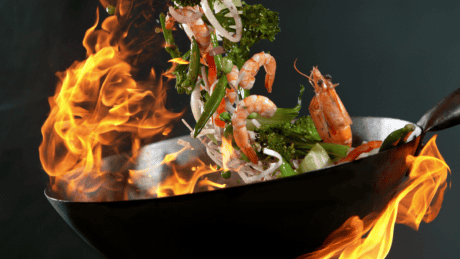 a wok with shrimp and vegetables being cooked