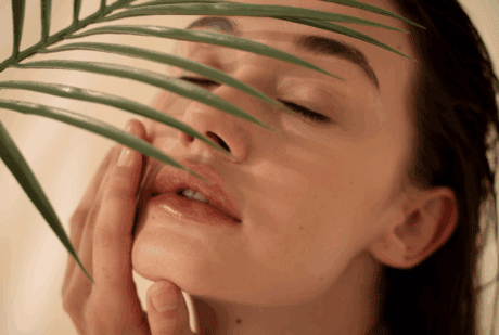 a woman with her eyes closed and a palm leaf behind her