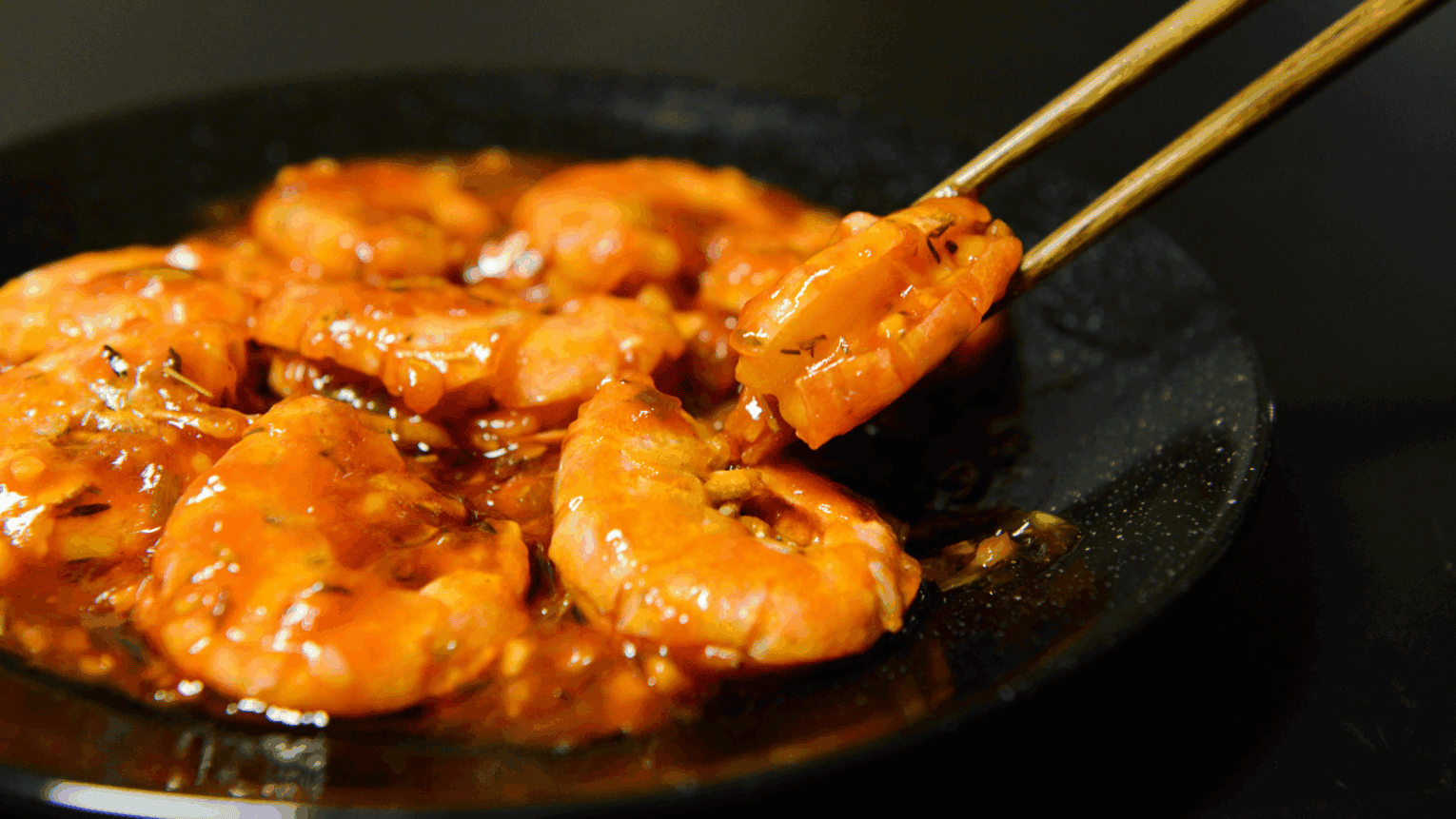 a pair of chopsticks holding shrimp in a pan