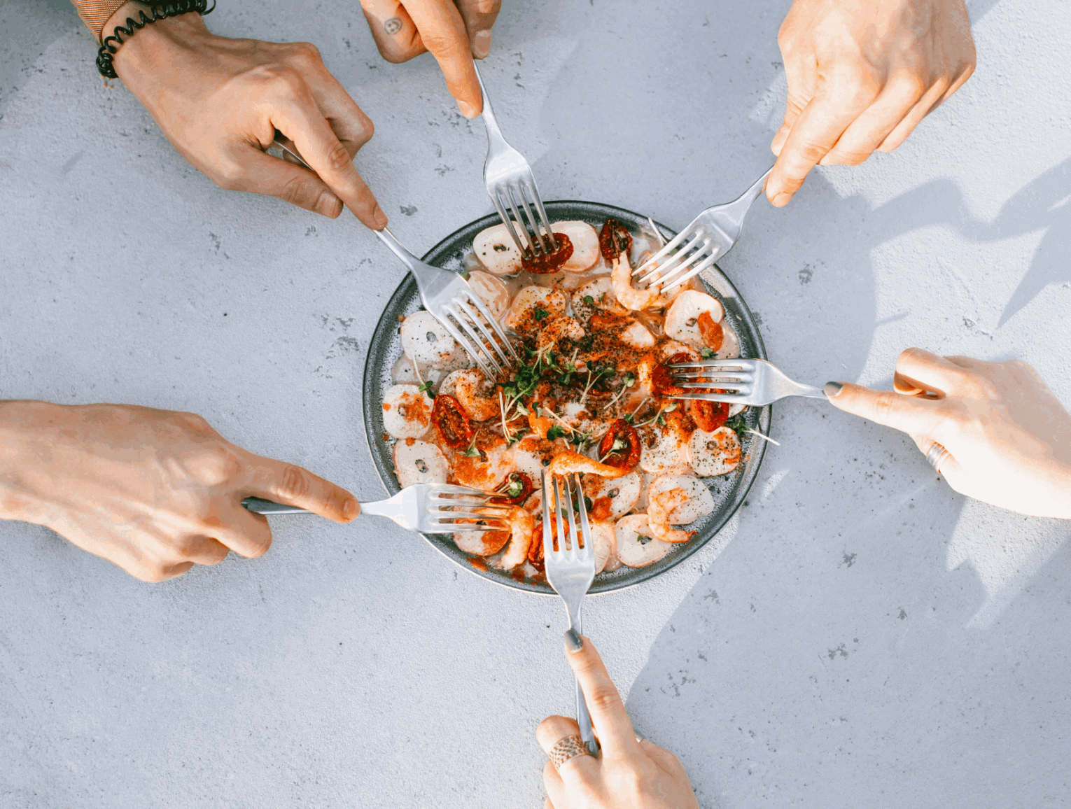 a group of hands holding forks over a plate of food