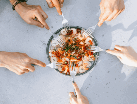 a group of hands holding forks over a plate of food