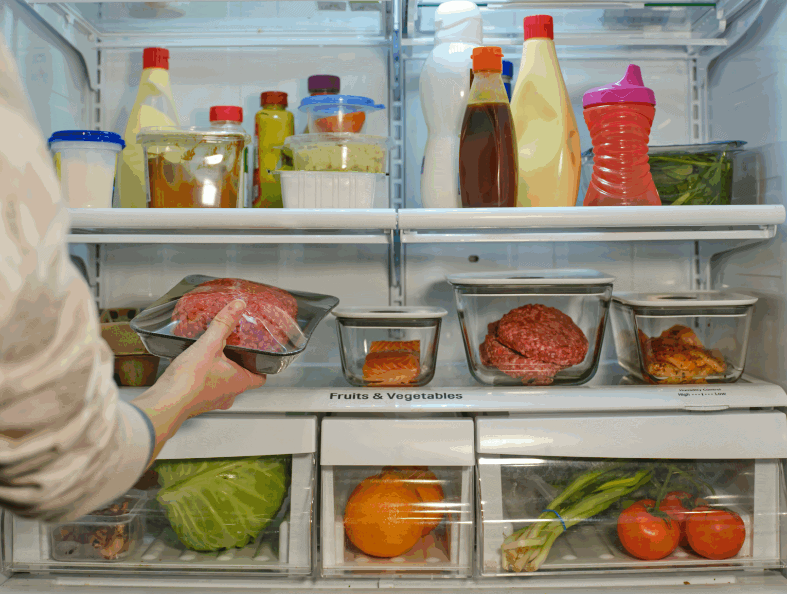 a person holding a tray of meat in a refrigerator
