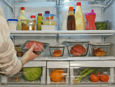 a person holding a tray of meat in a refrigerator